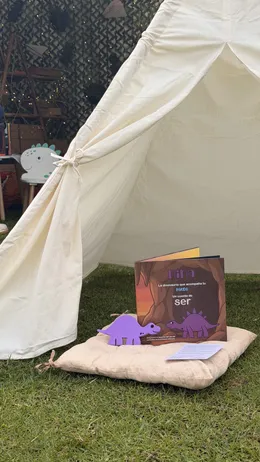 El cuento de Nina y su juguete sobre un cojín de piso, junto a un tipi en el jardín